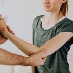 Crop unrecognizable chiropractor examining arm of smiling female patient