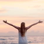 Rear View of Woman With Arms Raised at Beach during Sunset